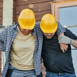 Construction working helping injured construction worker walk off job site.