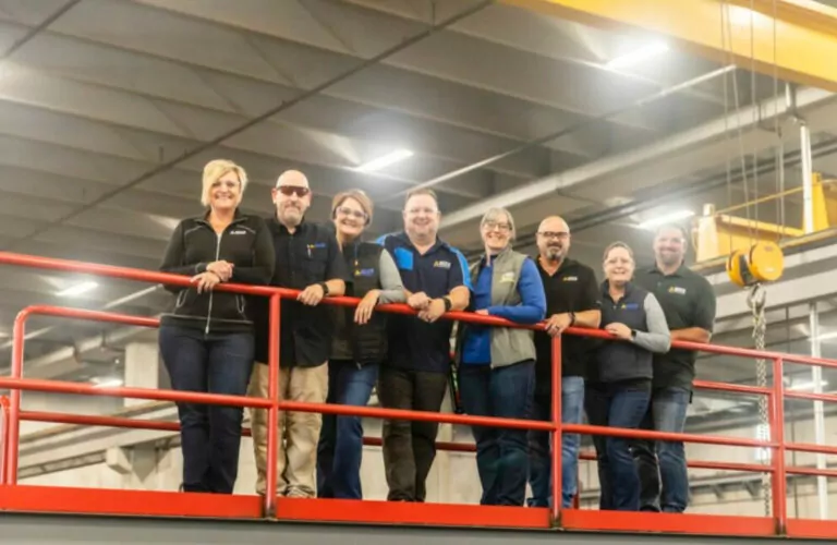 OECS safety instructors standing on safety rail in manufacturing building.