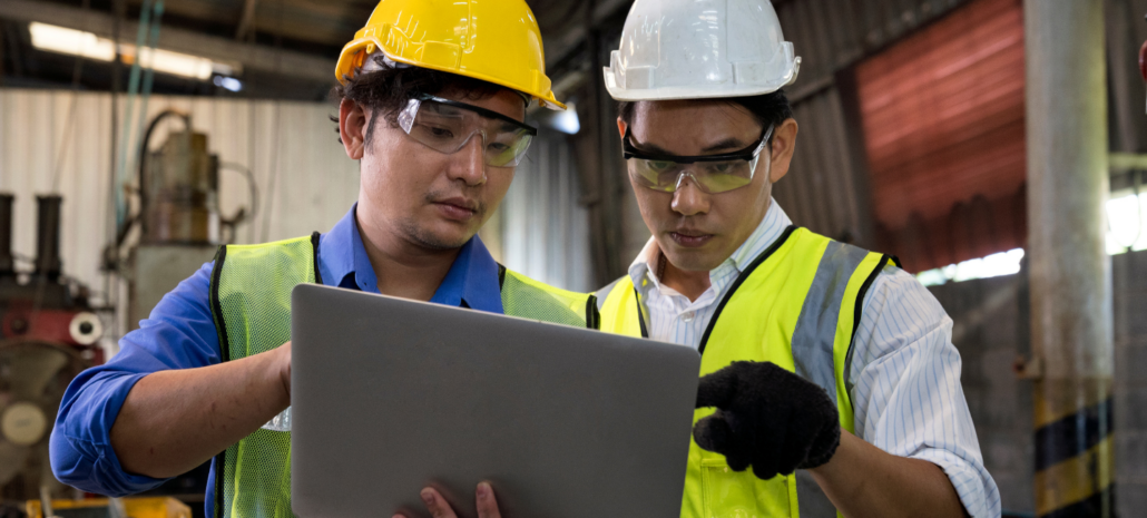 Two men with hardhats and safety glasses looking at a computer