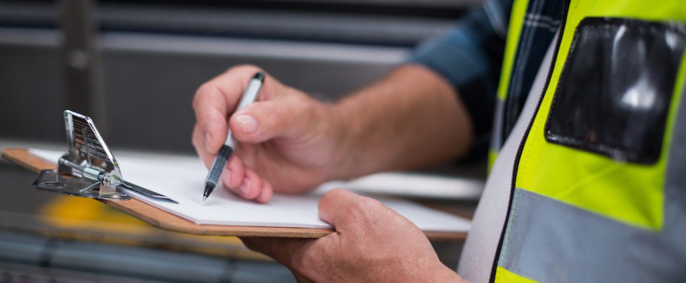 Mid section of male factory worker maintaining record on clipboard in drinks production factory