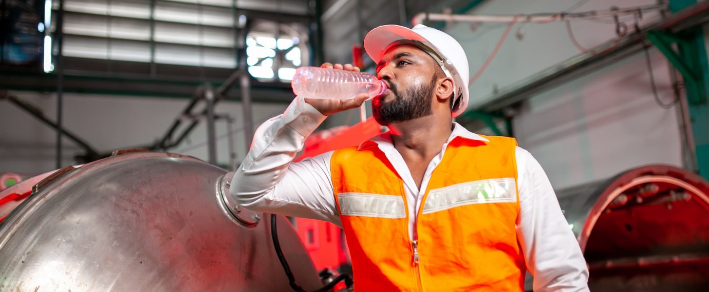 Professional engineers with helmets work to maintain industrial construction equipment. The worker is thirsty and drink refreshing water.