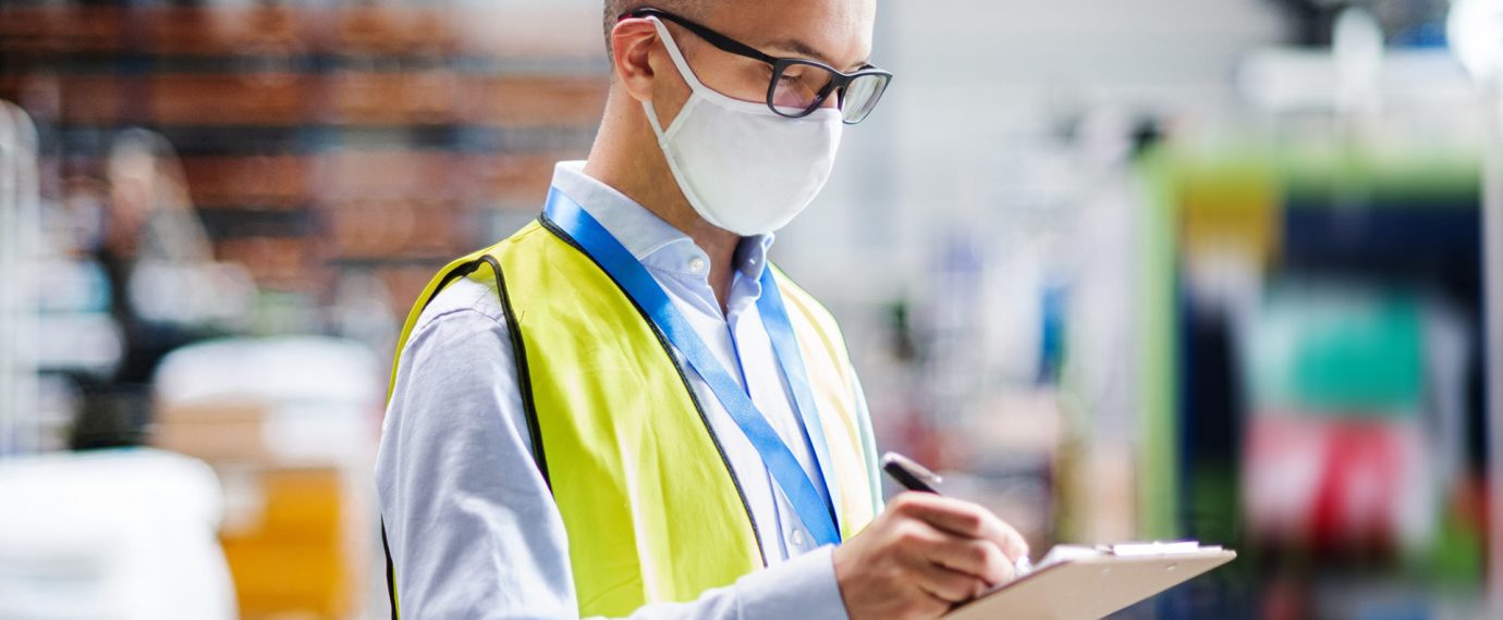 Portrait of technician or engineer with protective mask working in industrial factory, writing.