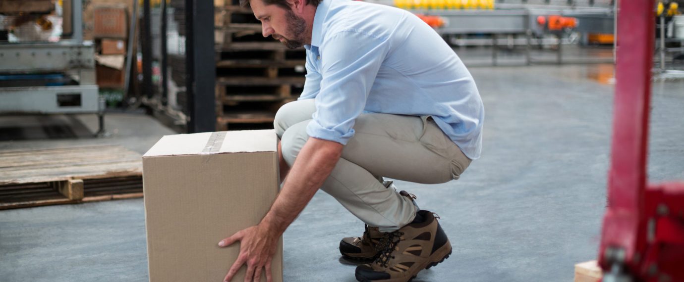 Attentive factory worker picking up cardboard boxes in factory